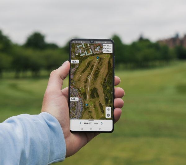 Male golfer holding mobile phone showing GPS hole view from Shot Scope app