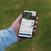 Male golfer holding mobile phone showing scorecard from Shot Scope app