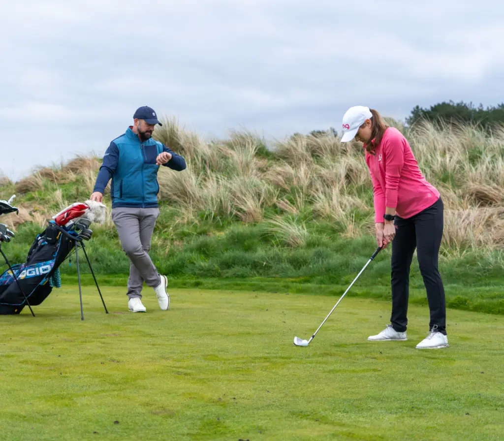 golfer on tee about to hit a shot with playing partner behind looking at shot scope gps watch