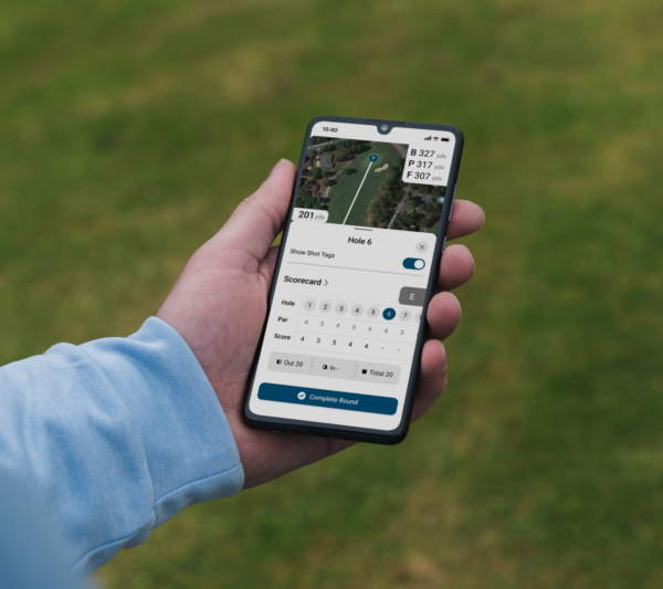 Male golfer holding mobile phone showing scorecard from Shot Scope app